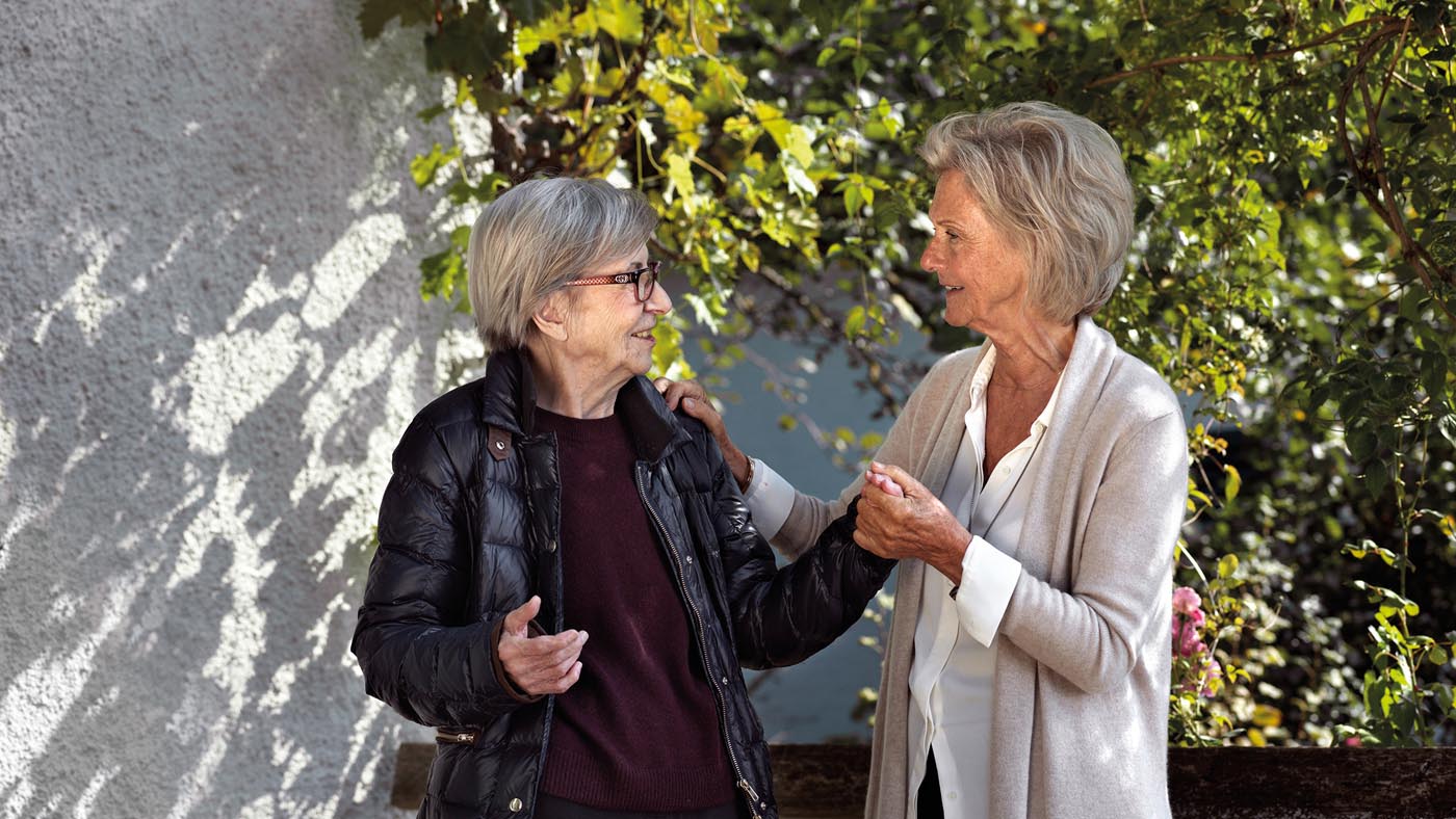 Zwei Seniorinnen schwatzen miteinander und halten sich an den Händen